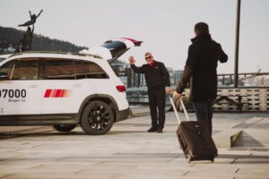 Person i 07000-uniform ønsker en reisende med koffert velkommen ved taxien